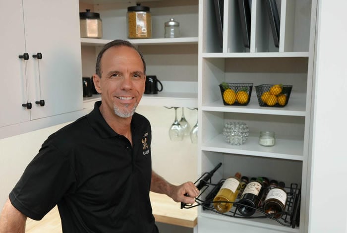 able-closet A man smiles in a pantry, holding a pull-out wine rack with bottles. Shelves behind him display lemons in baskets, jars, glasses, and a candle.