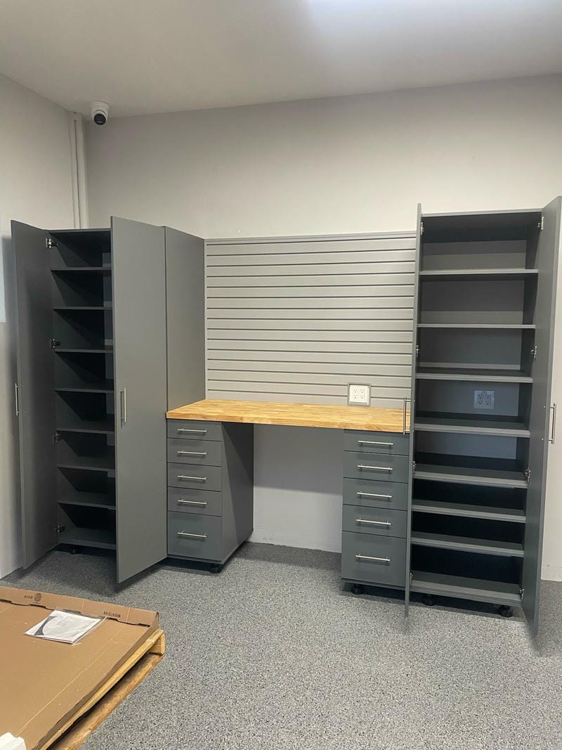 able-closet Gray storage cabinets and drawers with shelves are arranged around a wooden workbench in a clean, organized room with a slat wall panel and gray speckled flooring.
