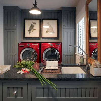 able-closet A stylish laundry room with dark gray cabinets, laundry room storage, a black countertop, red washer and dryer, a large sink, and two framed owl prints above the machines. Flowers and gardening tools rest on the counter near the sink.