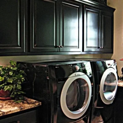 able-closet A laundry room with black cabinets providing ample laundry room storage, a front-loading washer and dryer, granite countertops, a potted plant, a red table lamp, and a window with a decorative valance letting in sunlight.